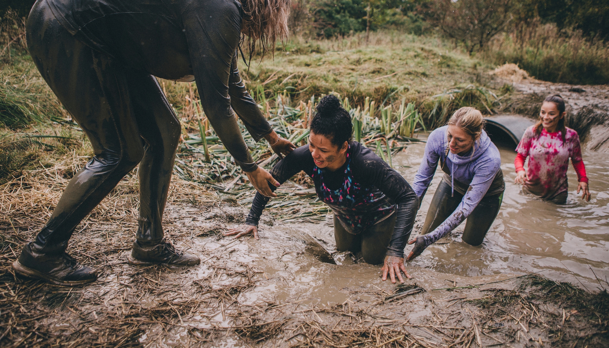 Women climb through mud obstacle at challenge event