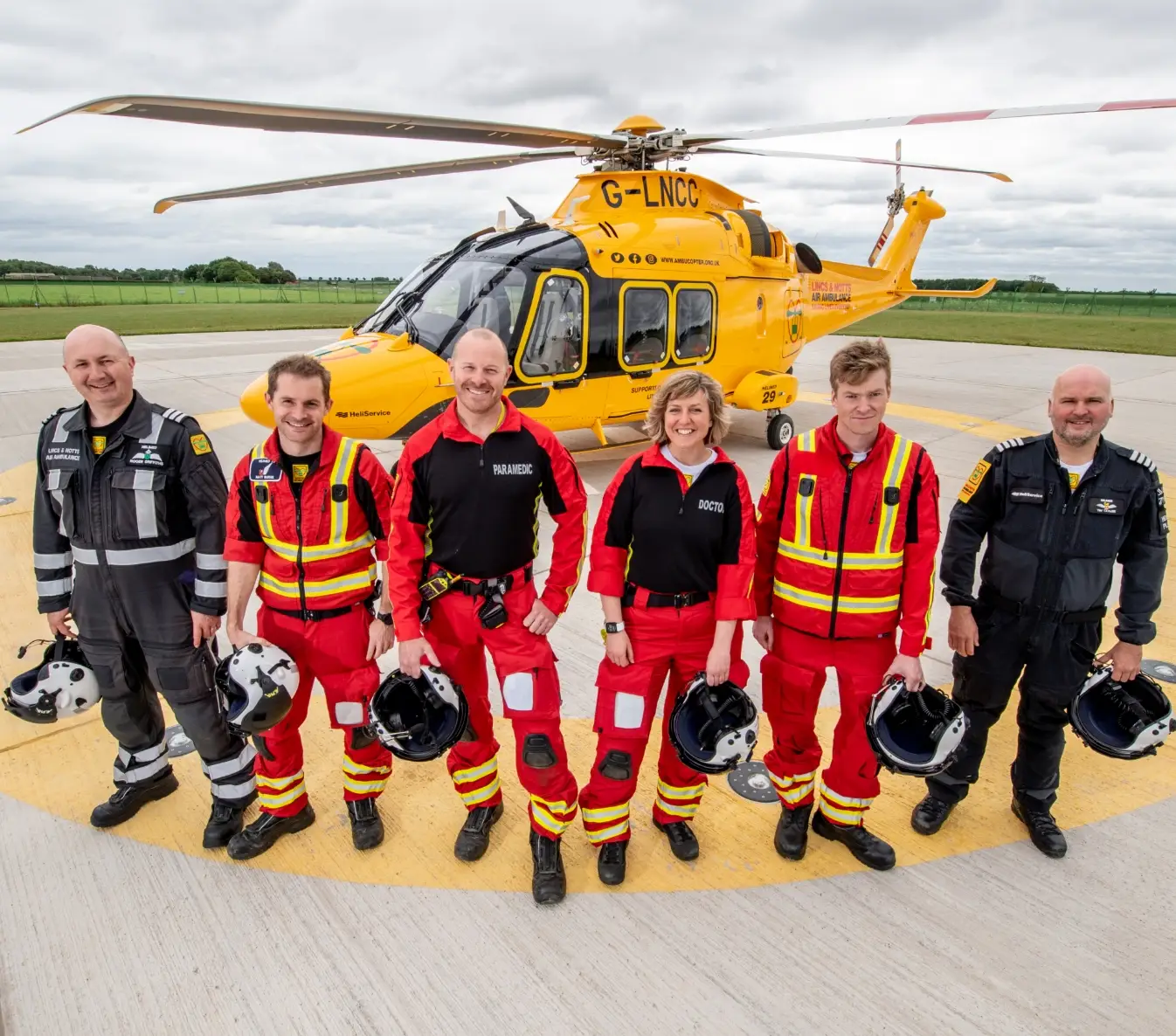 LNAA crew holding helmets in front of helicopter